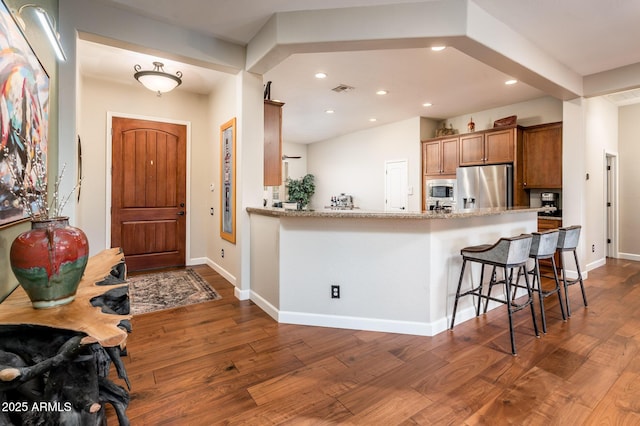 kitchen featuring a kitchen bar, dark wood-type flooring, kitchen peninsula, and appliances with stainless steel finishes