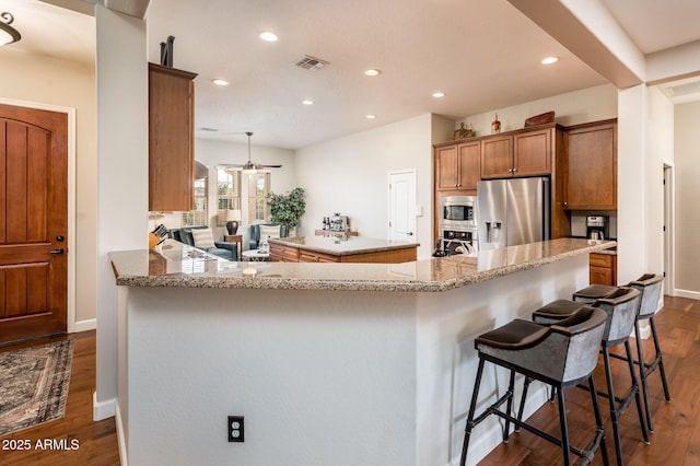 kitchen with a breakfast bar area, stainless steel appliances, dark hardwood / wood-style floors, light stone counters, and kitchen peninsula