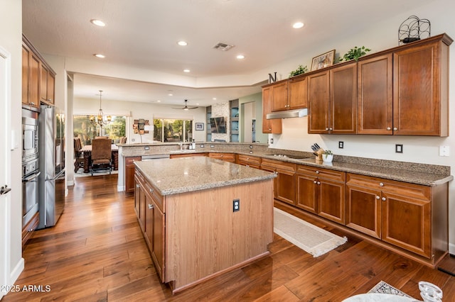 kitchen with dark wood-type flooring, hanging light fixtures, stainless steel appliances, a kitchen island, and kitchen peninsula