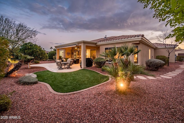 back house at dusk featuring a patio area and a lawn