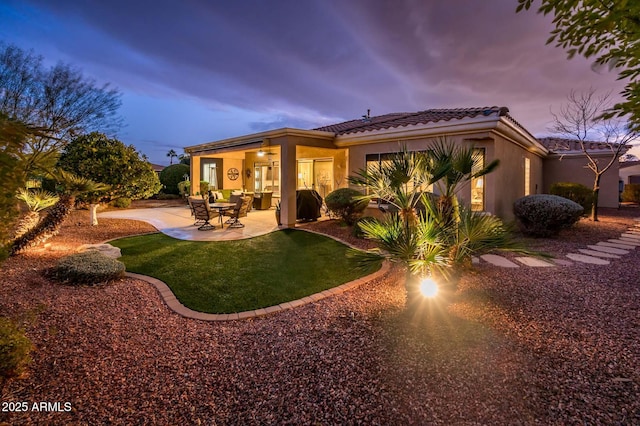 back house at dusk featuring a patio area and a lawn