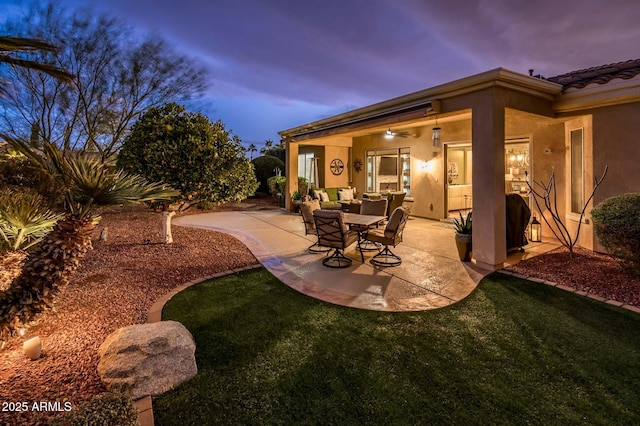 patio terrace at dusk featuring ceiling fan and a yard