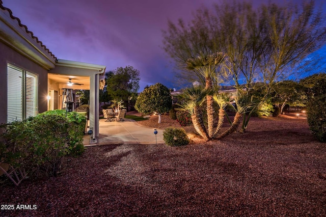 yard at dusk featuring ceiling fan and a patio