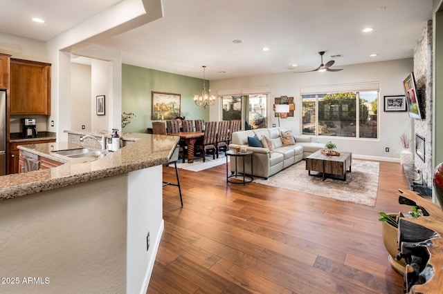 living room featuring ceiling fan with notable chandelier, sink, hardwood / wood-style floors, and a fireplace