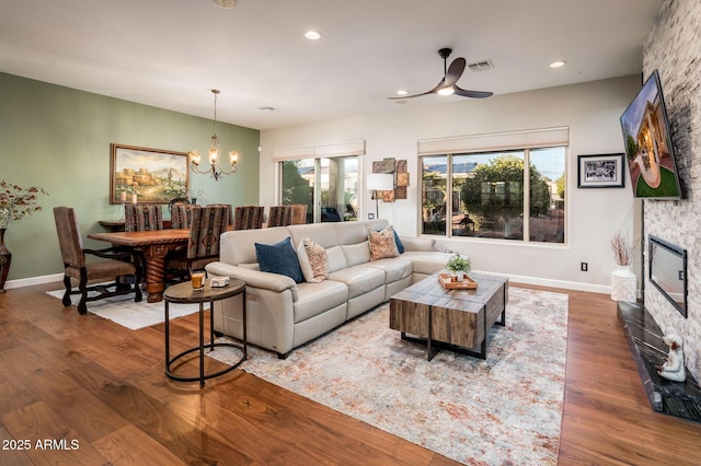 living room featuring ceiling fan with notable chandelier, a stone fireplace, and hardwood / wood-style floors