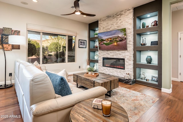 living room with hardwood / wood-style flooring, a stone fireplace, ceiling fan, and built in shelves