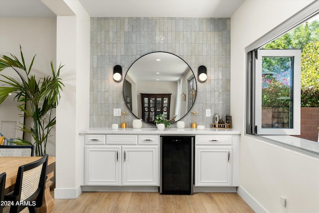 bar featuring light wood-type flooring, beverage cooler, and decorative backsplash