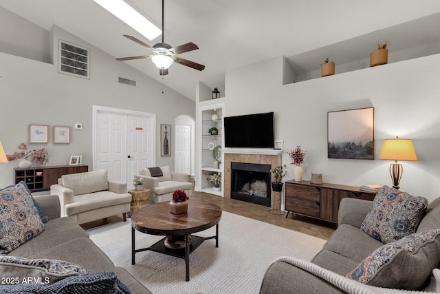 living room featuring high vaulted ceiling, built in features, a tile fireplace, and ceiling fan