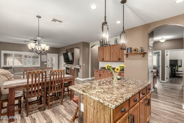 kitchen with light stone counters, brown cabinets, arched walkways, an inviting chandelier, and visible vents