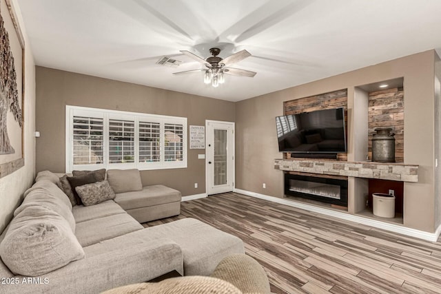 living room with wood finished floors, a glass covered fireplace, ceiling fan, baseboards, and visible vents