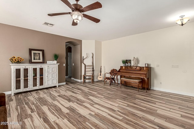 living area featuring visible vents, arched walkways, baseboards, light wood-style flooring, and ceiling fan