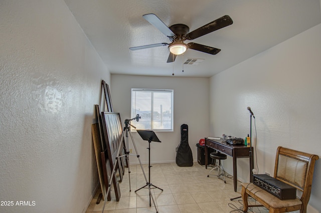 home office with light tile patterned floors, a ceiling fan, visible vents, baseboards, and a textured wall