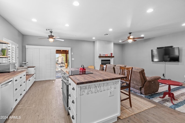 kitchen featuring wooden counters, a large fireplace, stainless steel appliances, white cabinets, and light hardwood / wood-style floors