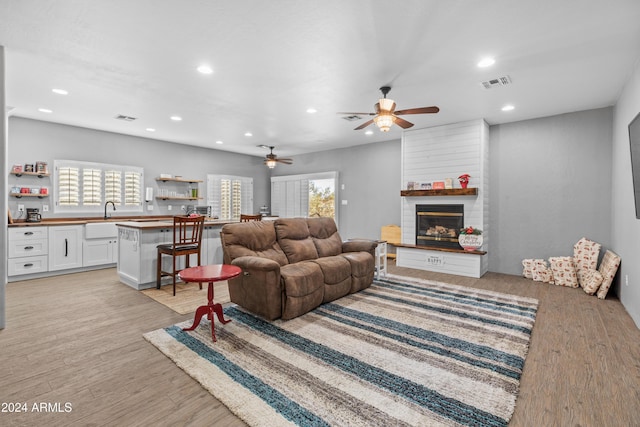 living room with ceiling fan, a large fireplace, sink, and light hardwood / wood-style flooring