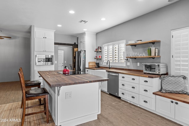 kitchen featuring butcher block counters, a center island, a barn door, white cabinets, and appliances with stainless steel finishes