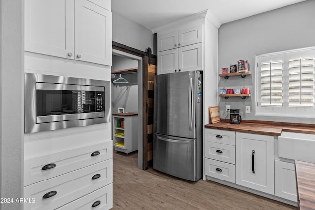 kitchen with white cabinetry, stainless steel appliances, wood counters, a barn door, and light wood-type flooring