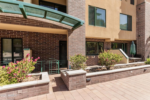 doorway to property featuring brick siding, a patio area, and stucco siding