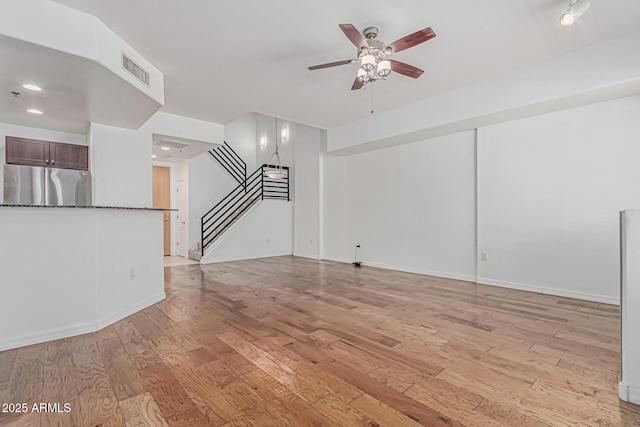 unfurnished living room featuring visible vents, baseboards, stairway, a ceiling fan, and light wood-style flooring