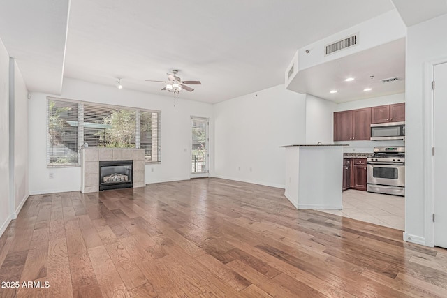 unfurnished living room featuring a ceiling fan, visible vents, light wood-style flooring, and a tile fireplace
