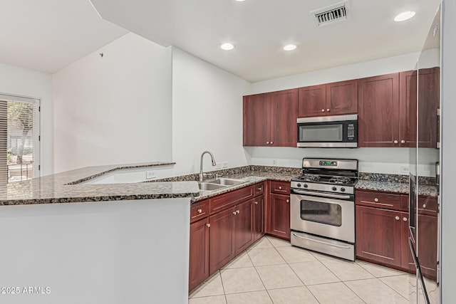 kitchen with a peninsula, dark brown cabinets, a sink, appliances with stainless steel finishes, and light tile patterned floors
