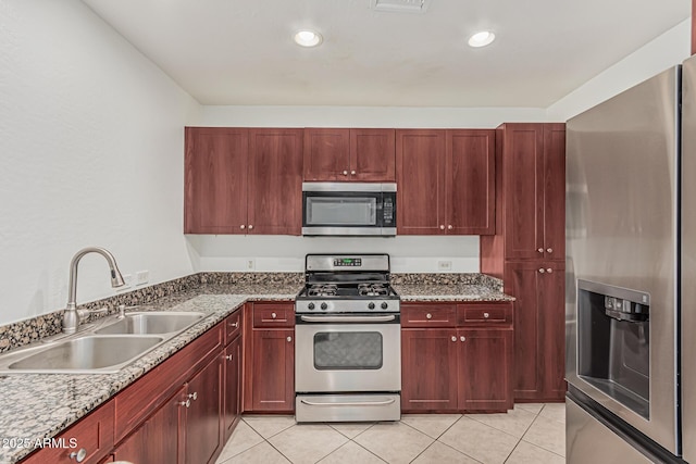 kitchen with dark brown cabinets, a sink, light tile patterned floors, dark stone countertops, and stainless steel appliances