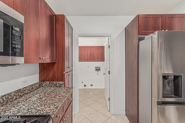 kitchen featuring dark stone countertops, light tile patterned floors, dark brown cabinets, and stainless steel appliances
