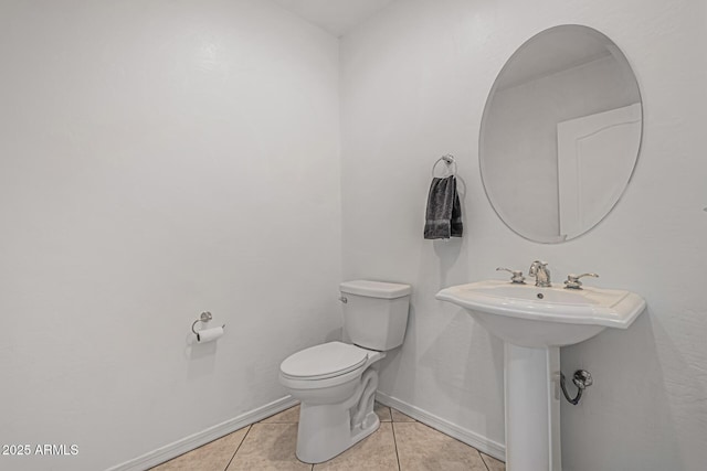 half bathroom with toilet, baseboards, a sink, and tile patterned flooring