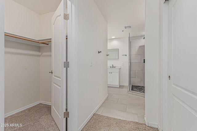 interior space featuring a walk in closet, visible vents, a shower stall, vanity, and baseboards