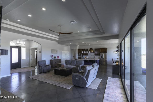 living room featuring ceiling fan with notable chandelier and a raised ceiling