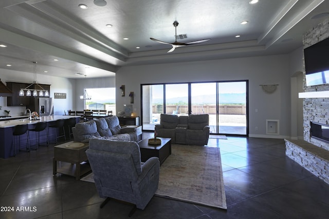 tiled living room featuring ceiling fan, a fireplace, and a tray ceiling