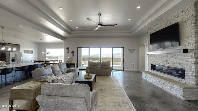 living room with a raised ceiling, a stone fireplace, ceiling fan, and concrete floors