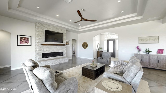 living room featuring a tray ceiling, ceiling fan, and a fireplace