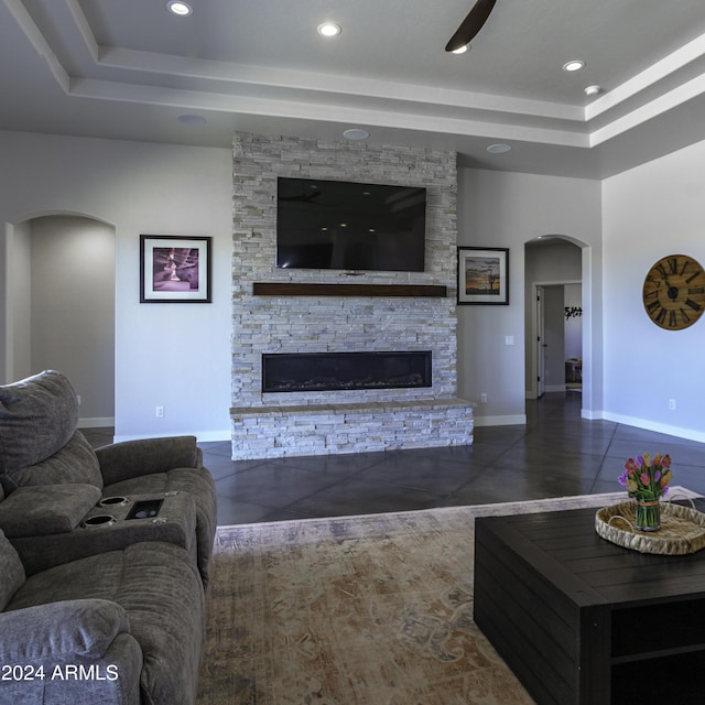 living room with ceiling fan, a stone fireplace, and dark tile patterned floors