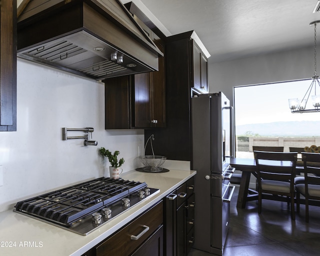 kitchen featuring wall chimney exhaust hood, stainless steel gas stovetop, dark brown cabinets, decorative light fixtures, and fridge