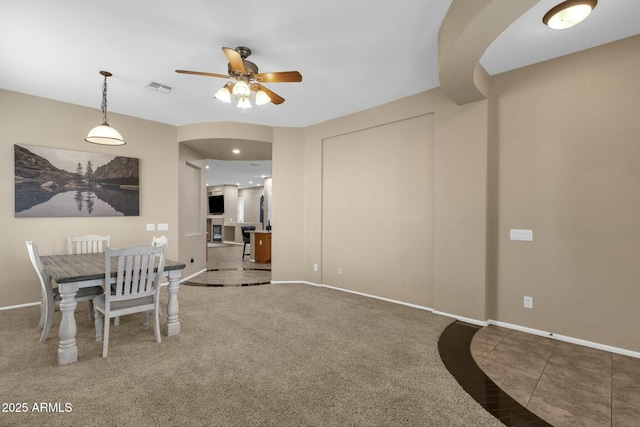 carpeted dining room featuring arched walkways, visible vents, tile patterned flooring, and baseboards