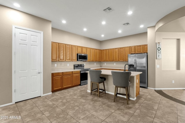 kitchen with stainless steel appliances, visible vents, a kitchen island with sink, and light countertops