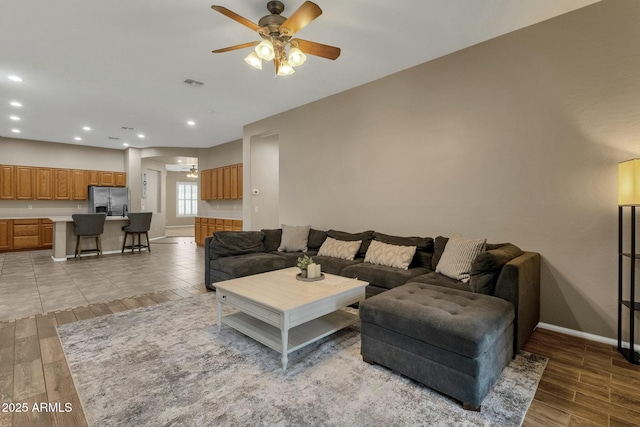 living room with wood finish floors, visible vents, baseboards, and ceiling fan