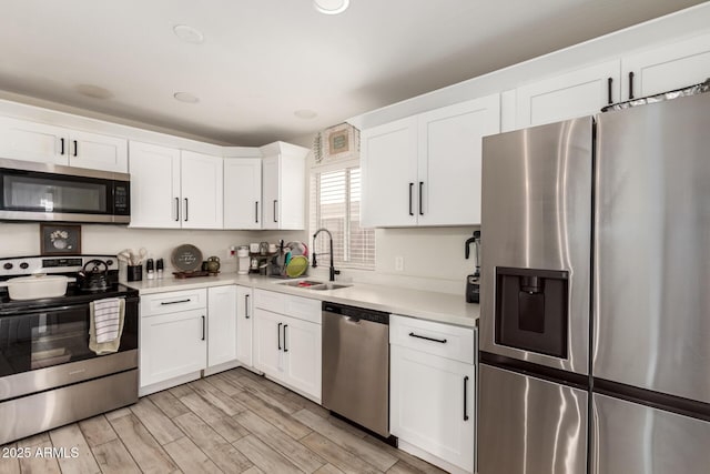 kitchen with stainless steel appliances, a sink, light countertops, white cabinets, and light wood-style floors