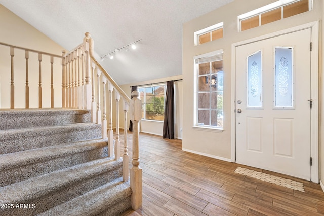 entryway featuring vaulted ceiling, rail lighting, and a textured ceiling