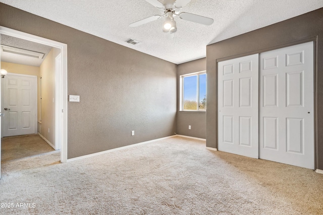 unfurnished bedroom featuring ceiling fan, light colored carpet, a textured ceiling, and a closet