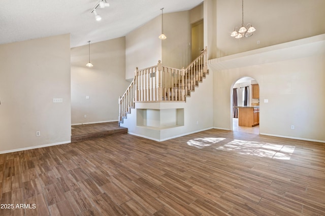 unfurnished living room with track lighting, high vaulted ceiling, a chandelier, and hardwood / wood-style floors