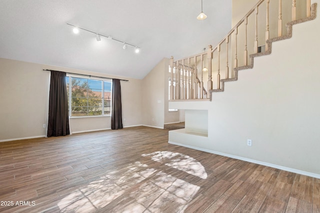 unfurnished living room featuring track lighting, lofted ceiling, and hardwood / wood-style floors