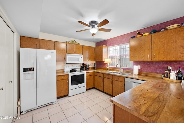 kitchen featuring light tile patterned floors, brown cabinets, white appliances, and a sink