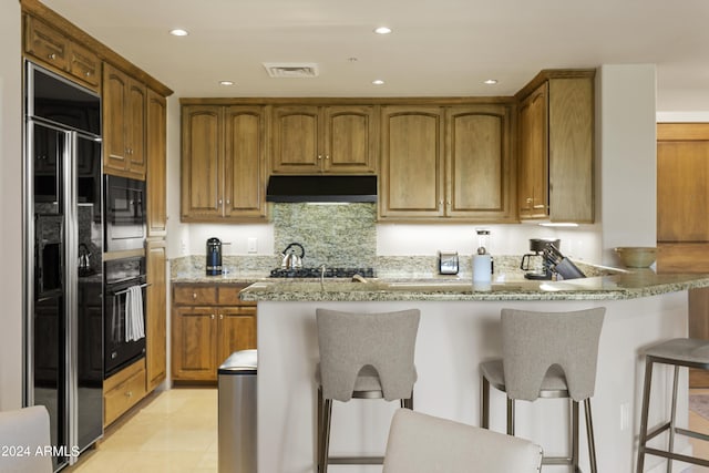 kitchen with tasteful backsplash, light stone counters, a breakfast bar, light tile patterned floors, and black appliances