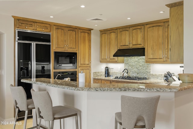 kitchen with light stone countertops, kitchen peninsula, a breakfast bar area, and black appliances