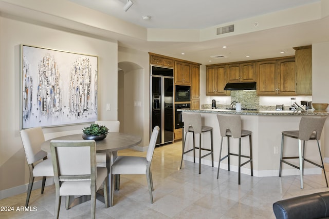 kitchen with kitchen peninsula, tasteful backsplash, a breakfast bar area, and black appliances