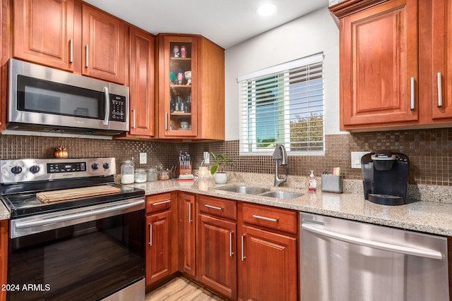 kitchen with backsplash, sink, light stone countertops, and stainless steel appliances