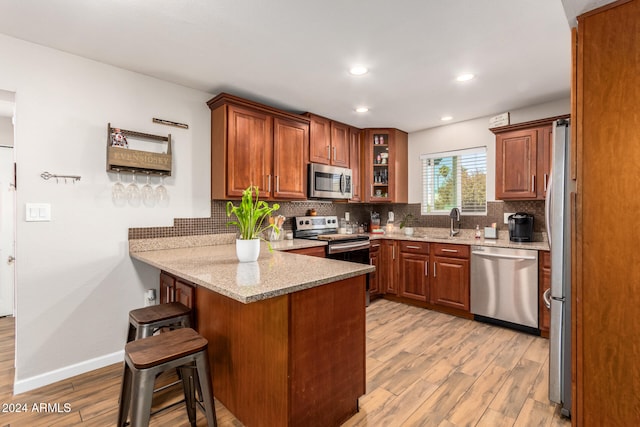 kitchen with kitchen peninsula, a kitchen bar, light stone countertops, stainless steel appliances, and light hardwood / wood-style flooring