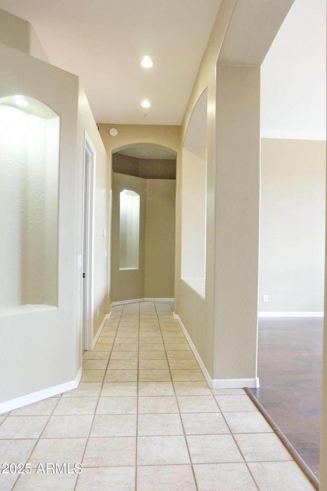 hallway with light tile patterned floors, recessed lighting, arched walkways, and baseboards