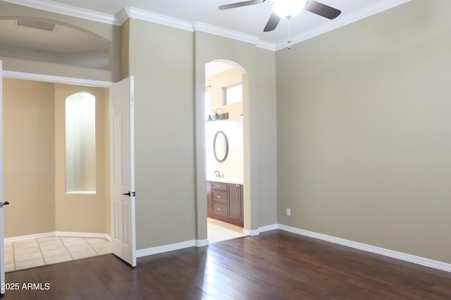 unfurnished bedroom with crown molding, wood finished floors, arched walkways, and baseboards